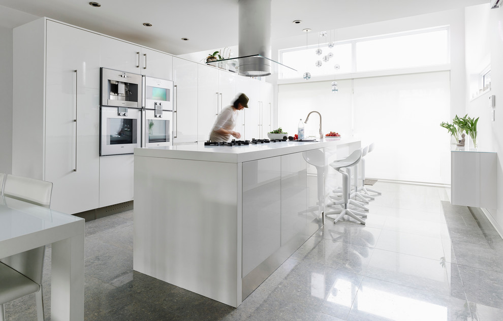 Modelo de cocina actual grande con armarios con paneles lisos, puertas de armario blancas, electrodomésticos blancos, suelo de cemento, una isla y fregadero bajoencimera