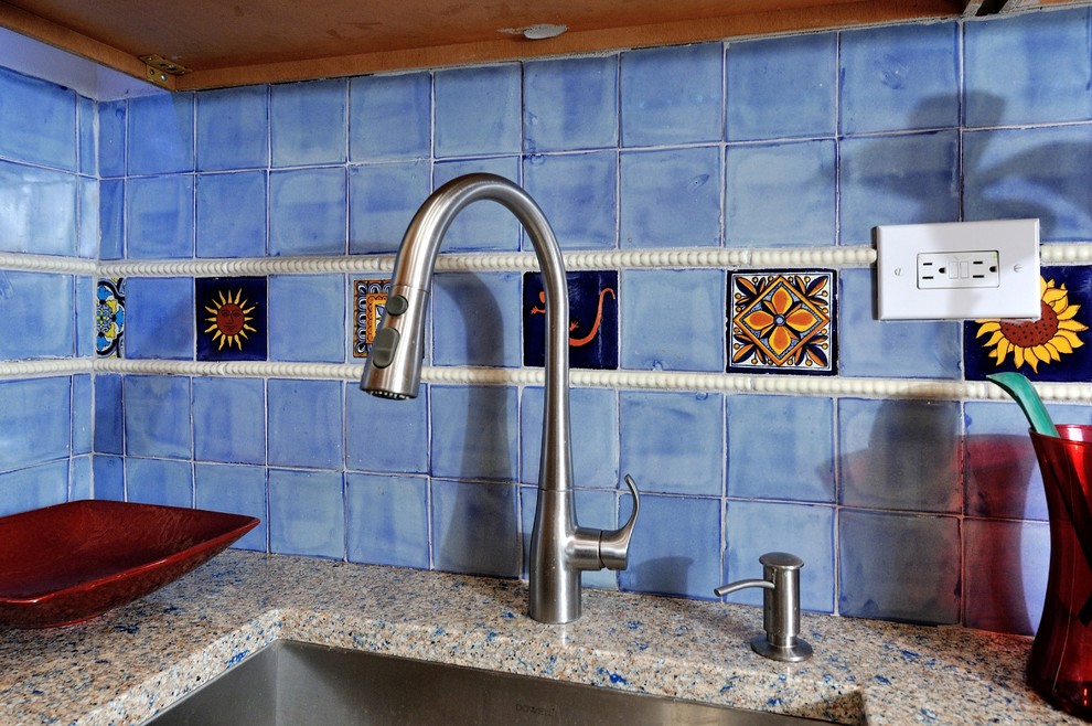 Cette photo montre une petite cuisine méditerranéenne en U et bois clair fermée avec un placard avec porte à panneau surélevé, une crédence bleue, une crédence en céramique, un électroménager en acier inoxydable, un évier encastré, un plan de travail en verre recyclé et un sol en carrelage de porcelaine.
