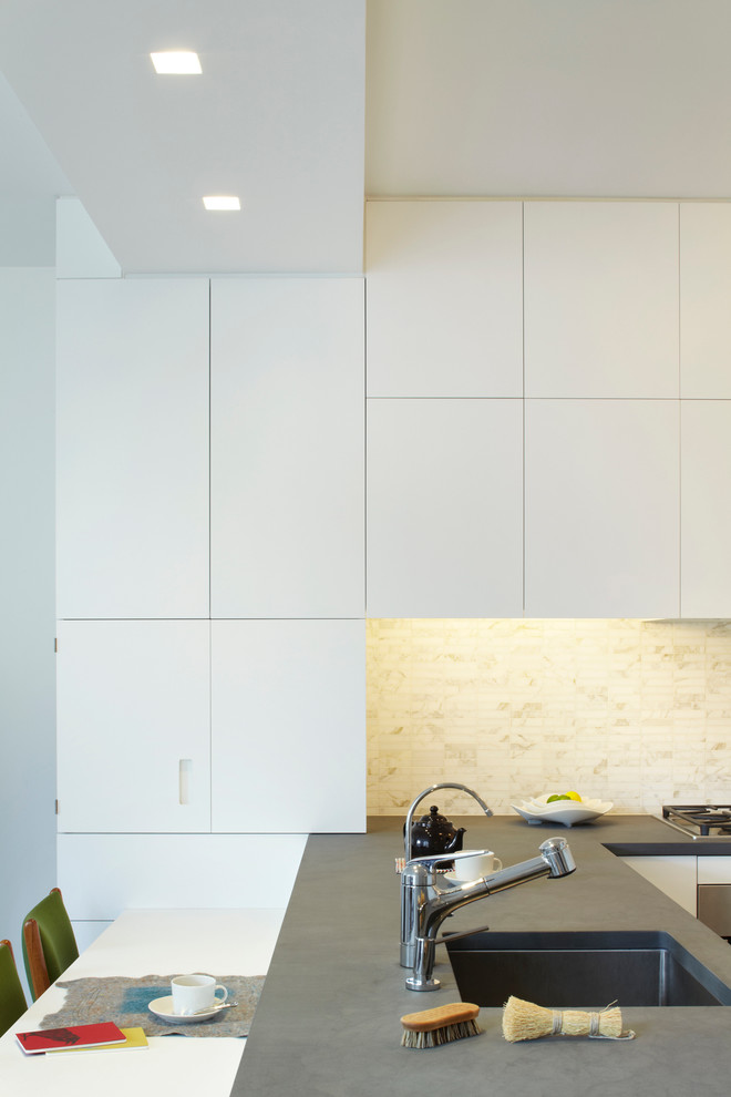 Inspiration for a small modern l-shaped medium tone wood floor eat-in kitchen remodel in New York with an undermount sink, flat-panel cabinets, white cabinets, limestone countertops, white backsplash, stone tile backsplash, stainless steel appliances and a peninsula
