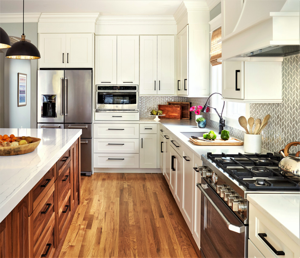 Medium sized farmhouse l-shaped open plan kitchen in DC Metro with a submerged sink, shaker cabinets, white cabinets, engineered stone countertops, grey splashback, porcelain splashback, integrated appliances, medium hardwood flooring, an island and white worktops.