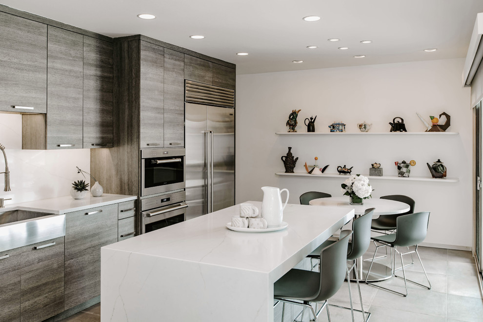 Photo of a medium sized contemporary l-shaped kitchen/diner in Detroit with a belfast sink, flat-panel cabinets, grey cabinets, engineered stone countertops, white splashback, stainless steel appliances, porcelain flooring, an island, grey floors and white worktops.
