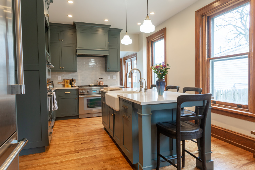 Inspiration for a mid-sized transitional l-shaped brown floor kitchen remodel in Philadelphia with a farmhouse sink, shaker cabinets, green cabinets, gray backsplash, stainless steel appliances, an island and gray countertops
