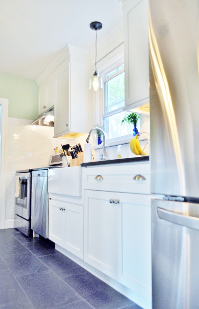 Bild på ett litet lantligt linjärt kök och matrum, med en rustik diskho, skåp i shakerstil, vita skåp, granitbänkskiva, vitt stänkskydd, stänkskydd i porslinskakel, rostfria vitvaror, skiffergolv och en köksö