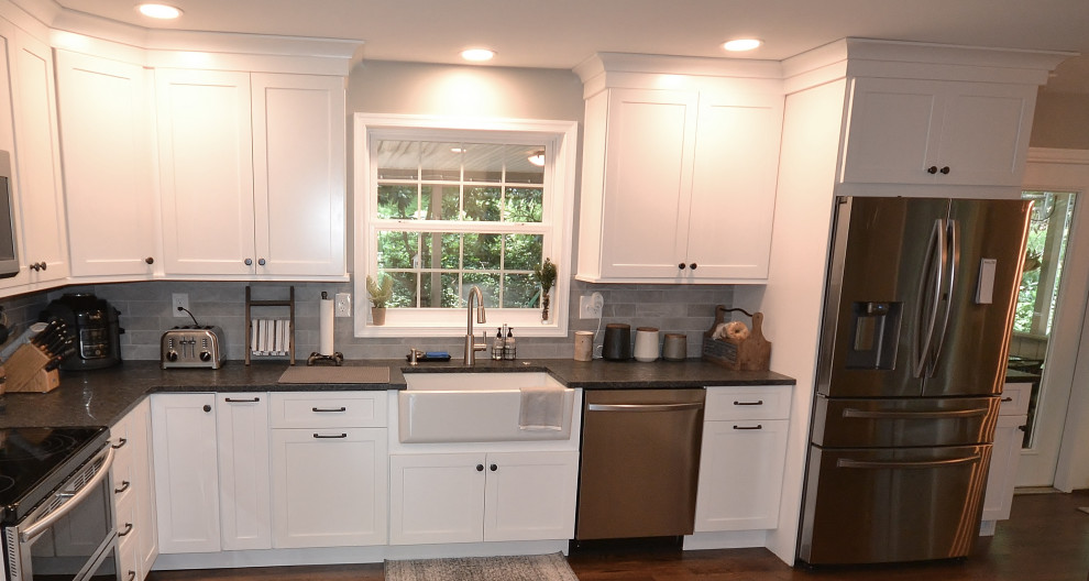 Photo of a large classic l-shaped kitchen/diner in Philadelphia with a belfast sink, recessed-panel cabinets, white cabinets, granite worktops, grey splashback, metro tiled splashback, stainless steel appliances, light hardwood flooring, a breakfast bar, brown floors and grey worktops.