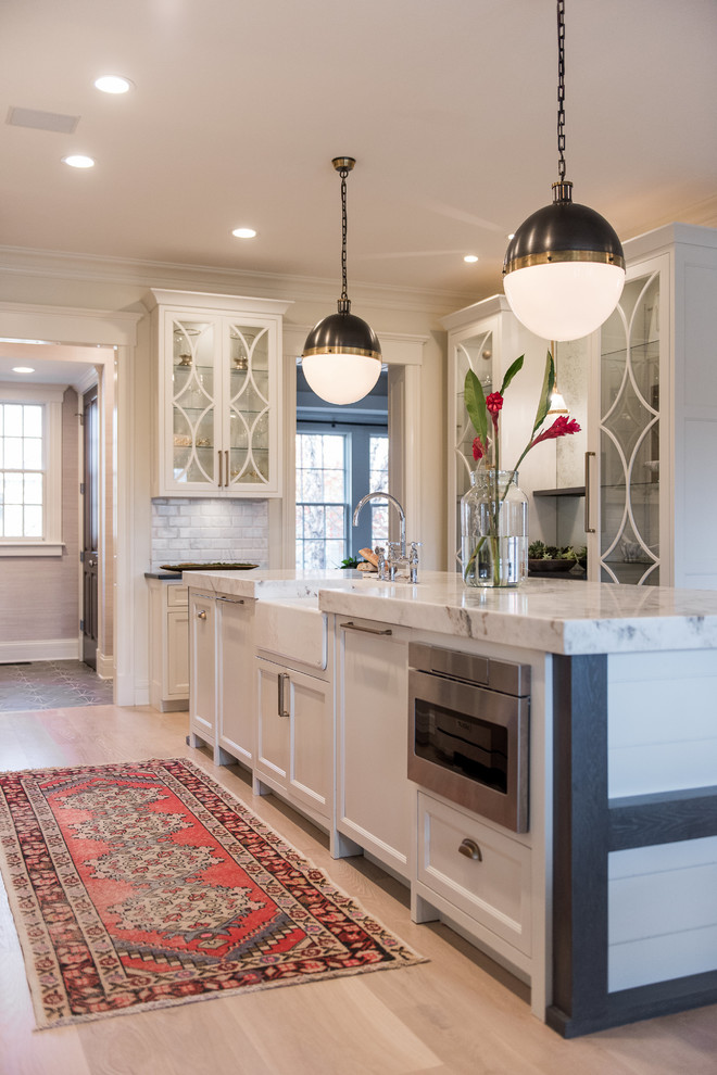 Inspiration for a classic kitchen in Indianapolis with a belfast sink, white cabinets, marble worktops, white splashback, marble splashback, stainless steel appliances, light hardwood flooring, an island, shaker cabinets and beige floors.