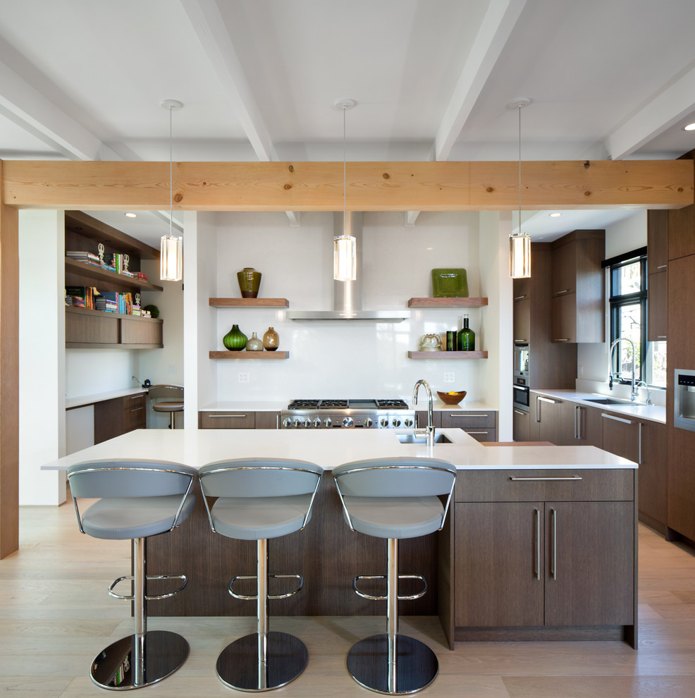 Moderne Küche mit Unterbauwaschbecken, flächenbündigen Schrankfronten, dunklen Holzschränken, Küchenrückwand in Weiß, Glasrückwand, Küchengeräten aus Edelstahl, hellem Holzboden und Kücheninsel in Vancouver