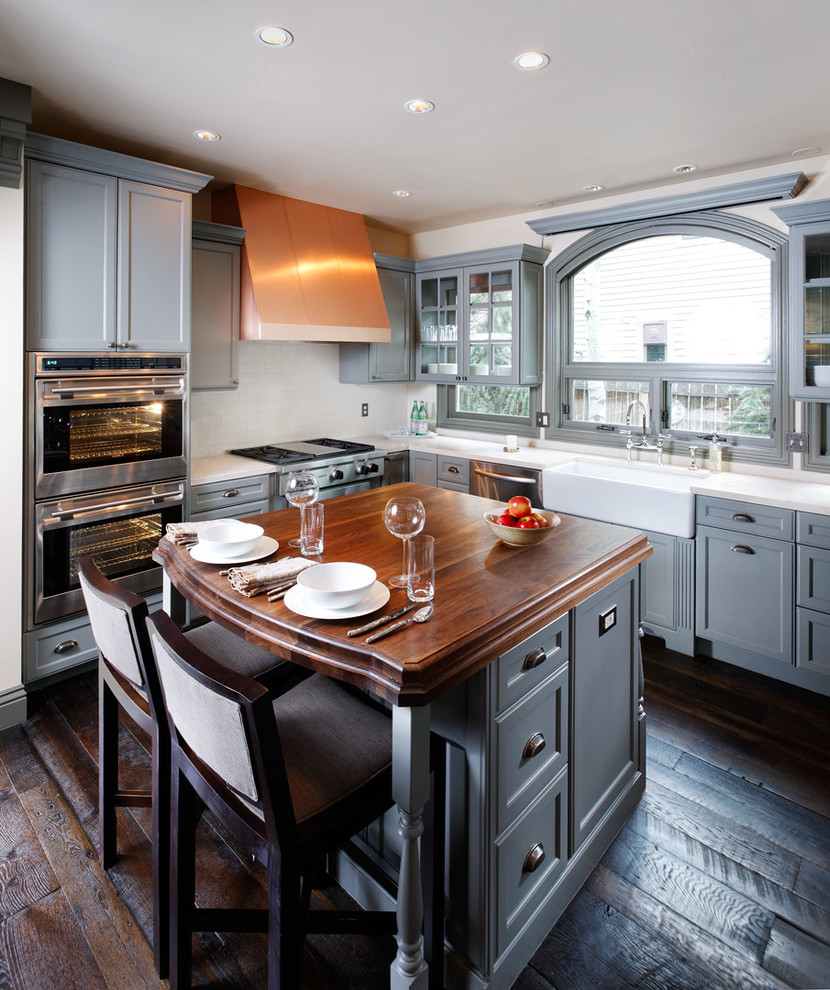 Example of a classic u-shaped eat-in kitchen design in Denver with a farmhouse sink, recessed-panel cabinets, gray cabinets, wood countertops, white backsplash, subway tile backsplash and stainless steel appliances