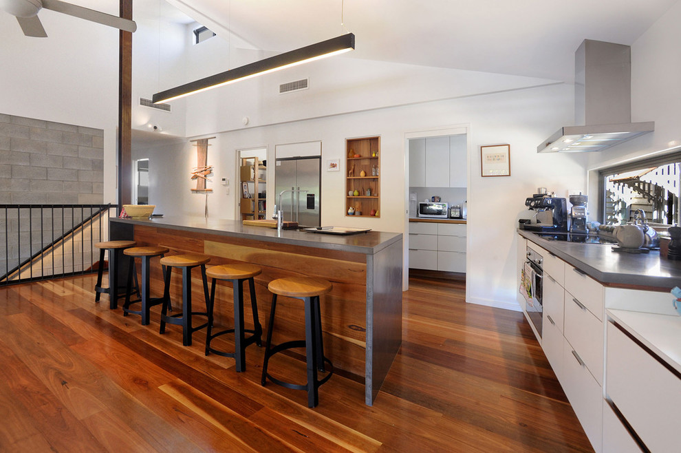 Mid-sized trendy l-shaped medium tone wood floor and brown floor kitchen photo in Townsville with a double-bowl sink, white cabinets, concrete countertops, stainless steel appliances, an island, flat-panel cabinets and gray countertops