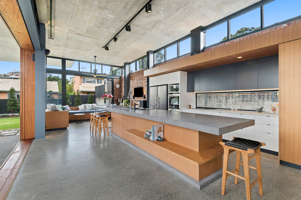 Foto på ett mycket stort industriellt grå kök, med bänkskiva i betong, betonggolv och en köksö