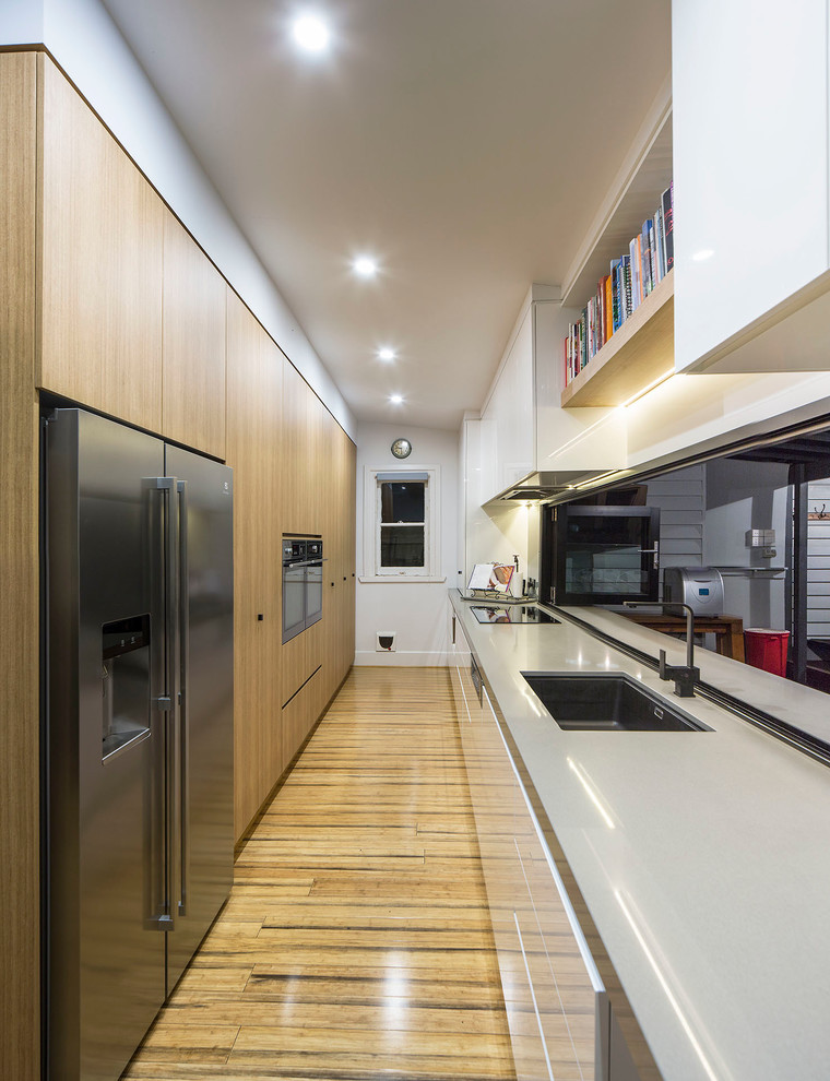 Стильный дизайн: большая, узкая параллельная кухня в современном стиле с врезной мойкой, плоскими фасадами и паркетным полом среднего тона - последний тренд