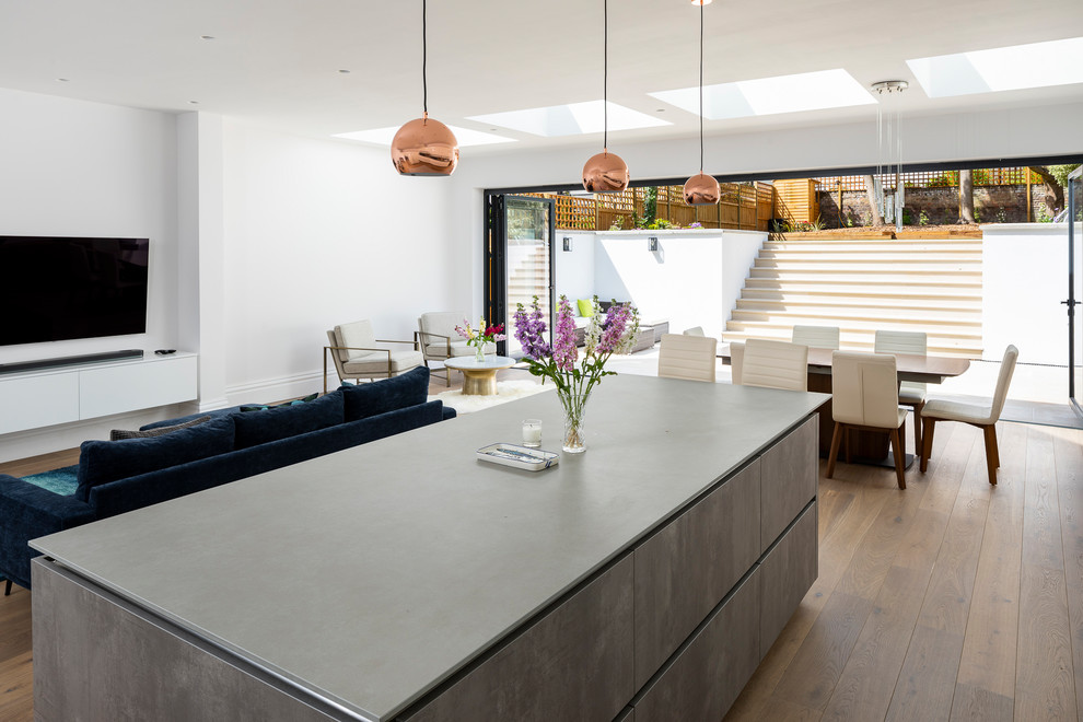 Large modern grey and brown l-shaped kitchen/diner in London with a submerged sink, flat-panel cabinets, white cabinets, concrete worktops, blue splashback, glass tiled splashback, integrated appliances, medium hardwood flooring, an island, brown floors, grey worktops and feature lighting.