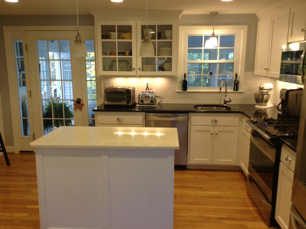Moderne Küche in L-Form mit Glasfronten, weißen Schränken, braunem Holzboden, Kücheninsel und Küchengeräten aus Edelstahl in New York