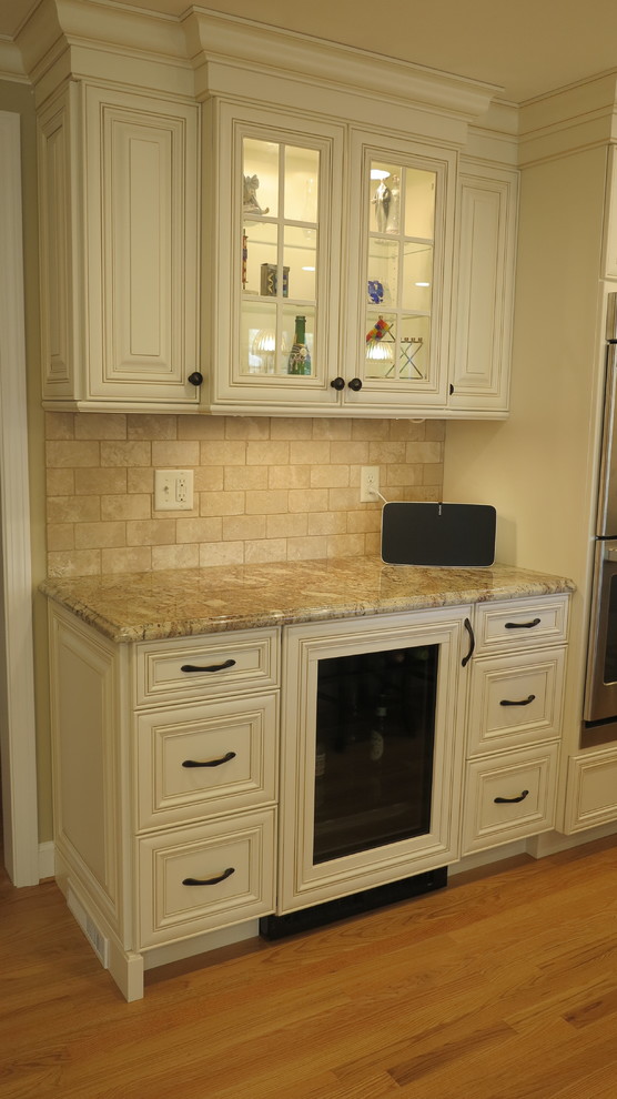 Inredning av ett klassiskt stort kök och matrum, med en undermonterad diskho, vita skåp, granitbänkskiva, beige stänkskydd, rostfria vitvaror, mellanmörkt trägolv och en köksö