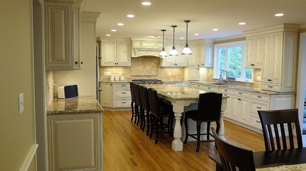 Inredning av ett klassiskt stort kök, med en undermonterad diskho, vita skåp, granitbänkskiva, beige stänkskydd, stänkskydd i stenkakel, rostfria vitvaror, mellanmörkt trägolv och en köksö