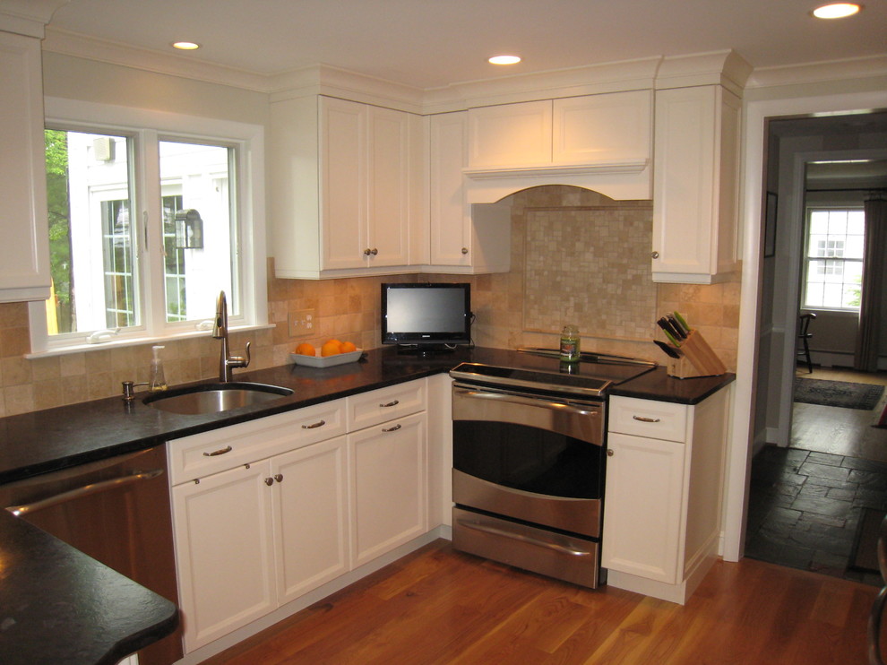 Inspiration for a mid-sized transitional u-shaped medium tone wood floor eat-in kitchen remodel in Bridgeport with an undermount sink, recessed-panel cabinets, white cabinets, granite countertops, beige backsplash, stone tile backsplash, stainless steel appliances, a peninsula and black countertops