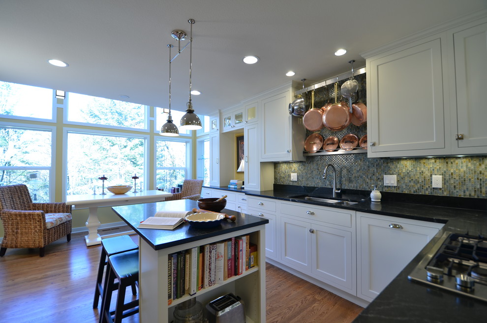 Example of a mid-sized l-shaped light wood floor eat-in kitchen design in Portland with an undermount sink, shaker cabinets, white cabinets, soapstone countertops, green backsplash, glass tile backsplash, stainless steel appliances and an island