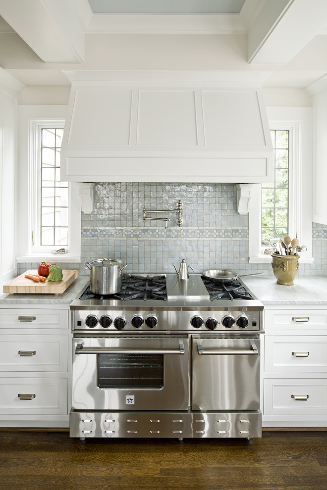 Cette photo montre une cuisine chic avec un électroménager en acier inoxydable, des portes de placard blanches, plan de travail en marbre et une crédence bleue.