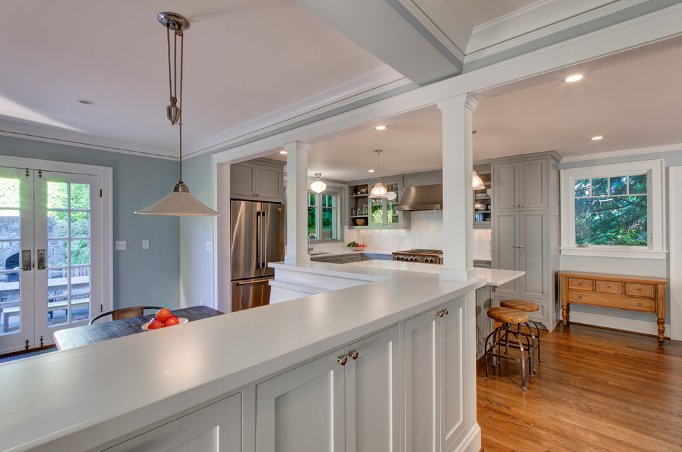 Foto de cocina clásica con puertas de armario grises, salpicadero blanco, electrodomésticos de acero inoxidable, suelo de madera en tonos medios y una isla