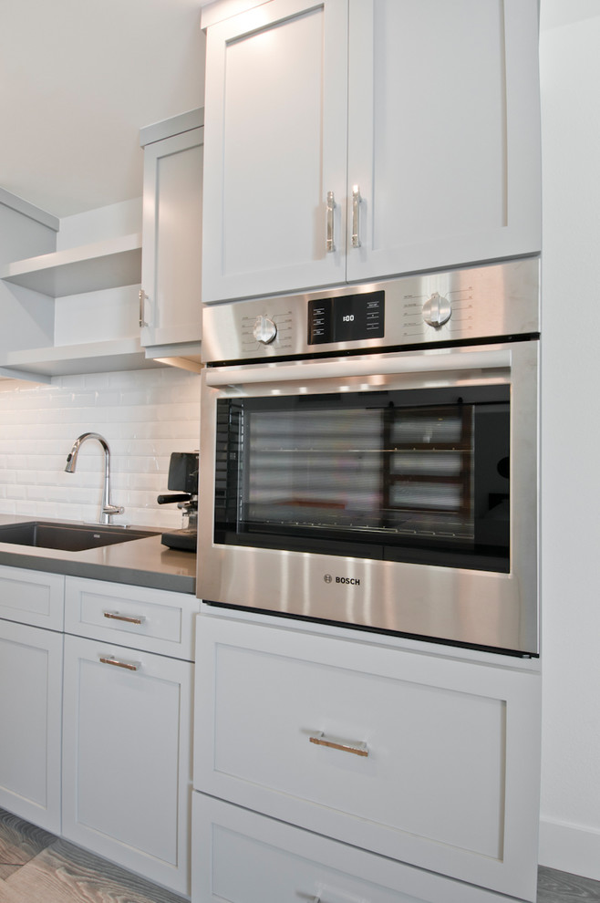 Inredning av ett klassiskt litet grå grått kök, med en undermonterad diskho, skåp i shakerstil, vita skåp, bänkskiva i kvarts, grått stänkskydd, stänkskydd i porslinskakel, rostfria vitvaror, mellanmörkt trägolv, en köksö och brunt golv