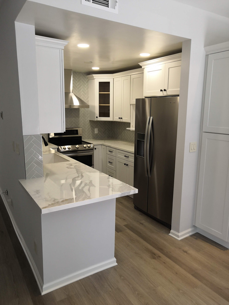 Inredning av ett modernt litet vit vitt kök, med en enkel diskho, luckor med infälld panel, vita skåp, träbänkskiva, grått stänkskydd, stänkskydd i tunnelbanekakel, rostfria vitvaror, vinylgolv, en halv köksö och grått golv