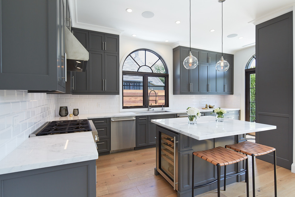Example of a mid-sized transitional l-shaped light wood floor open concept kitchen design in Los Angeles with a single-bowl sink, recessed-panel cabinets, gray cabinets, marble countertops, white backsplash, porcelain backsplash, stainless steel appliances and an island