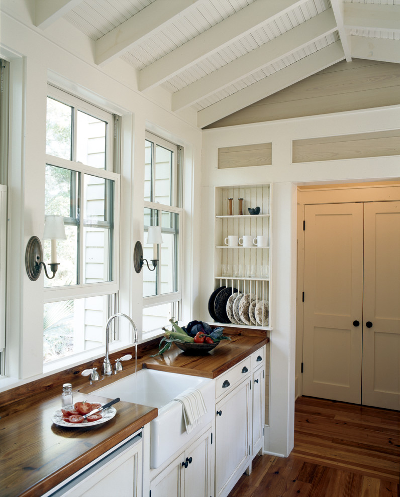 Exemple d'une cuisine chic avec un évier de ferme, un placard à porte affleurante, des portes de placard blanches et un plan de travail en bois.