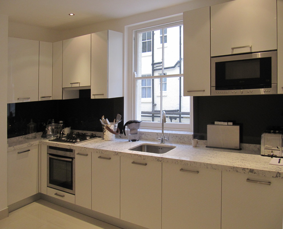 Inspiration for a small contemporary l-shaped enclosed kitchen in London with a single-bowl sink, flat-panel cabinets, white cabinets, composite countertops, black splashback, glass sheet splashback, stainless steel appliances, porcelain flooring and no island.
