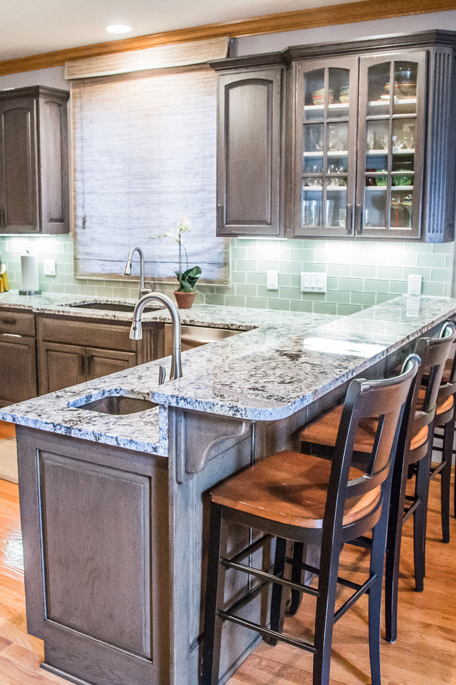 Inspiration for a large timeless u-shaped light wood floor eat-in kitchen remodel in Omaha with an undermount sink, glass-front cabinets, distressed cabinets, granite countertops, green backsplash, porcelain backsplash, stainless steel appliances and a peninsula