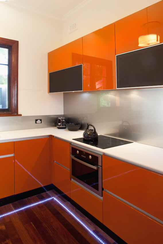 Exempel på ett mellanstort modernt grå grått kök, med en integrerad diskho, släta luckor, orange skåp, bänkskiva i koppar, stänkskydd med metallisk yta, glaspanel som stänkskydd, rostfria vitvaror och mörkt trägolv
