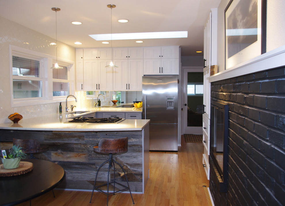 Example of a small trendy u-shaped light wood floor eat-in kitchen design in Portland with an undermount sink, shaker cabinets, white cabinets, solid surface countertops, white backsplash, subway tile backsplash, stainless steel appliances and a peninsula