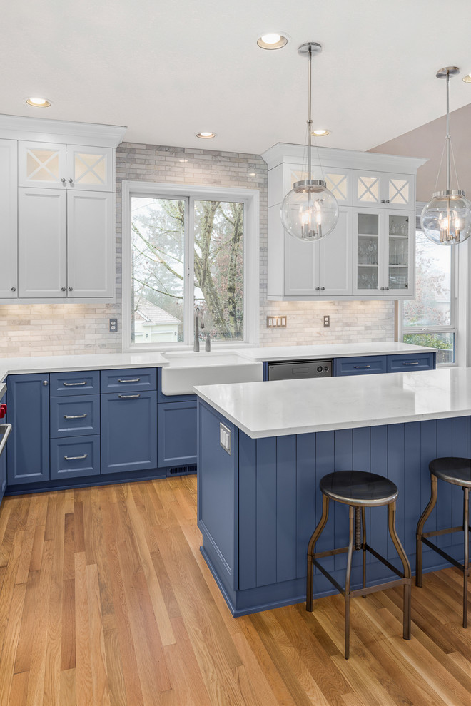 Inredning av ett klassiskt mellanstort kök, med en rustik diskho, luckor med infälld panel, blå skåp, bänkskiva i kvarts, vitt stänkskydd, stänkskydd i marmor, rostfria vitvaror, klinkergolv i porslin och en köksö