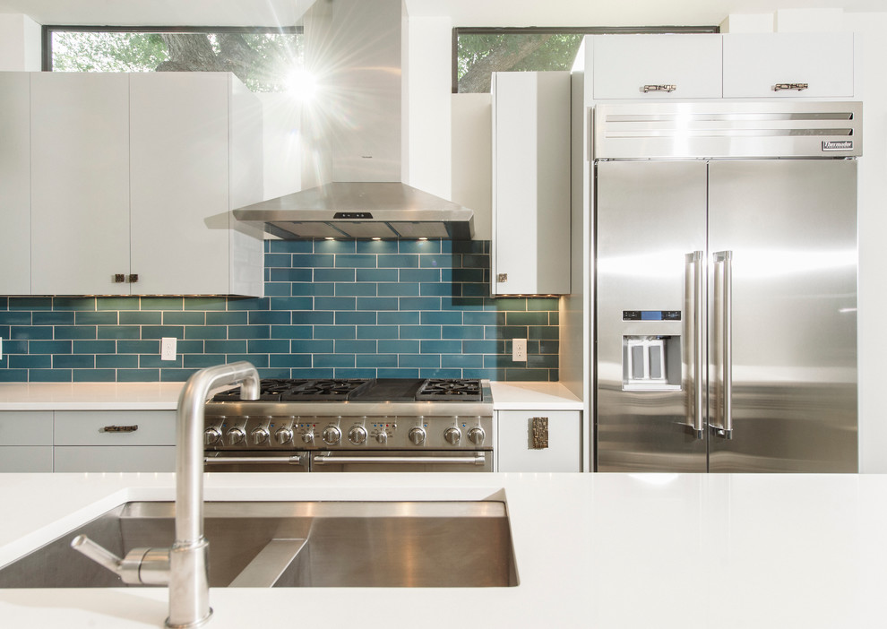 1950s concrete floor kitchen photo in Austin with an undermount sink, flat-panel cabinets, white cabinets, quartz countertops, blue backsplash, subway tile backsplash, stainless steel appliances and an island