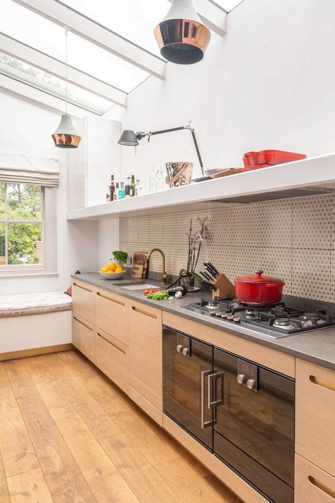Moderne Küche mit Unterbauwaschbecken, flächenbündigen Schrankfronten, hellen Holzschränken, Küchenrückwand in Beige, schwarzen Elektrogeräten, braunem Holzboden, braunem Boden und grauer Arbeitsplatte in London