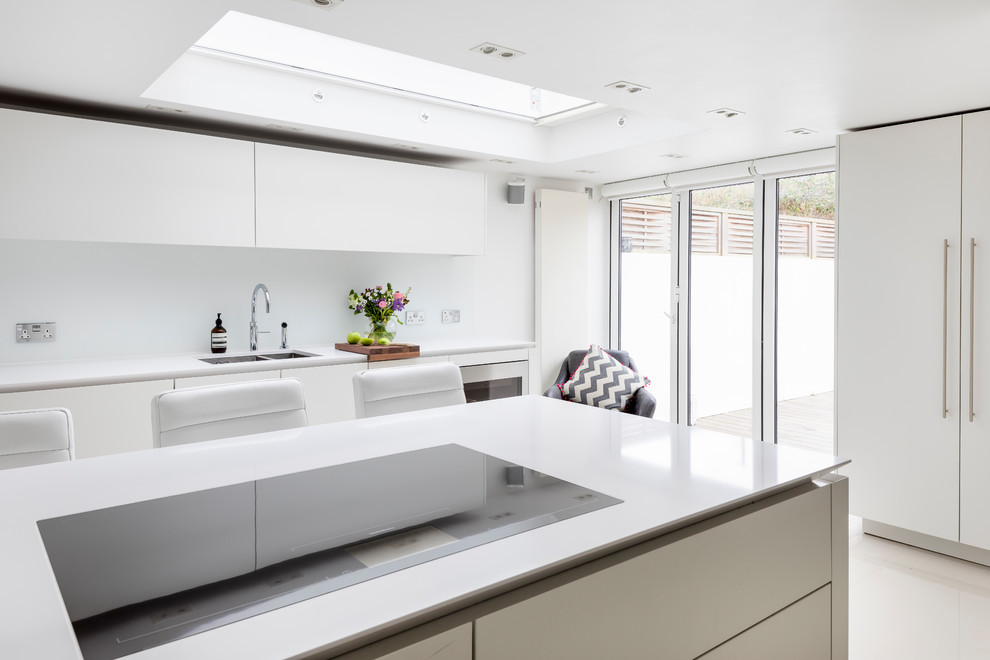 Photo of a medium sized contemporary galley enclosed kitchen in London with a built-in sink, flat-panel cabinets, white cabinets, white splashback, glass tiled splashback, stainless steel appliances, porcelain flooring, an island and white floors.