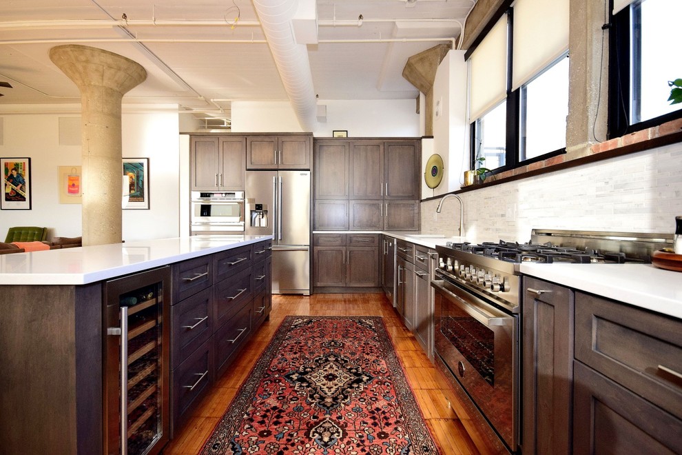 Photo of a large urban u-shaped kitchen/diner in Chicago with a built-in sink, recessed-panel cabinets, dark wood cabinets, granite worktops, white splashback, terracotta splashback, stainless steel appliances, medium hardwood flooring, an island and brown floors.