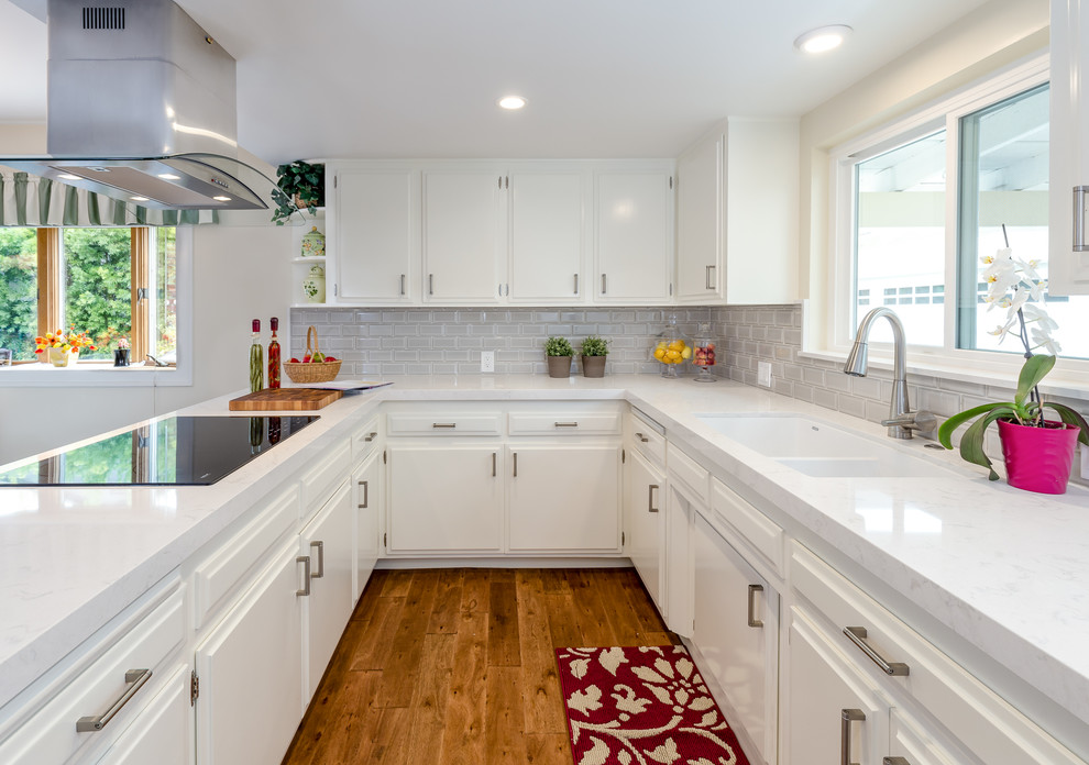 Modern inredning av ett mellanstort kök, med en undermonterad diskho, vita skåp, bänkskiva i kvarts, grått stänkskydd, stänkskydd i tunnelbanekakel, rostfria vitvaror, mellanmörkt trägolv och en halv köksö