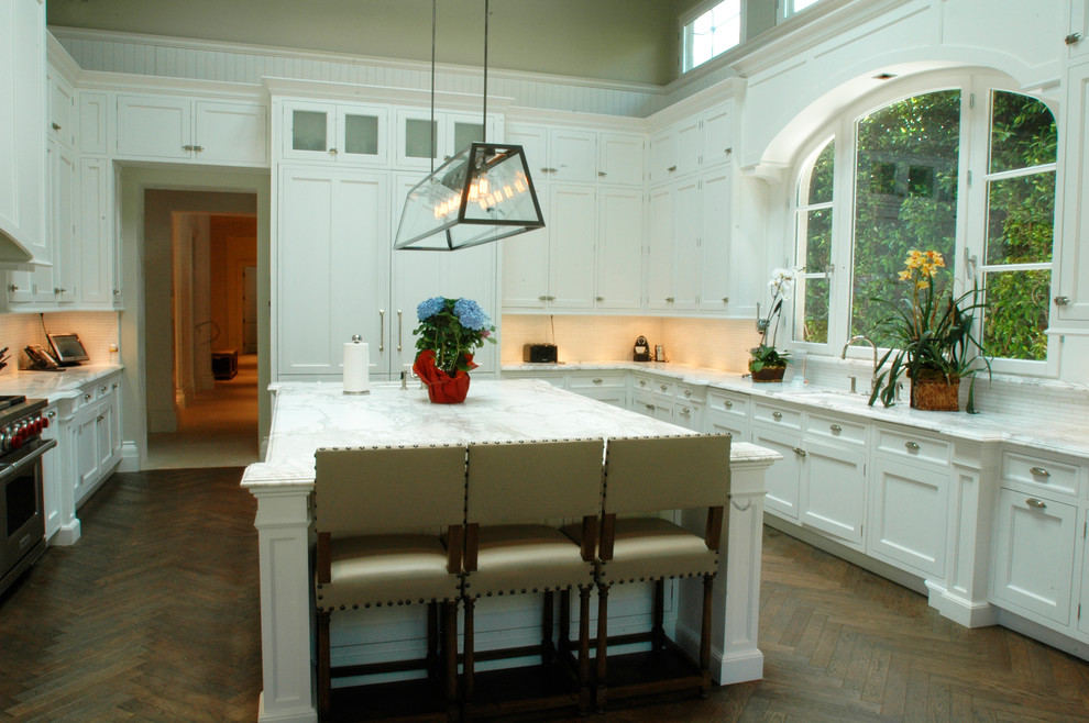 Large traditional u-shaped kitchen/diner in Los Angeles with a submerged sink, recessed-panel cabinets, white cabinets, marble worktops, white splashback, stone slab splashback, dark hardwood flooring and an island.