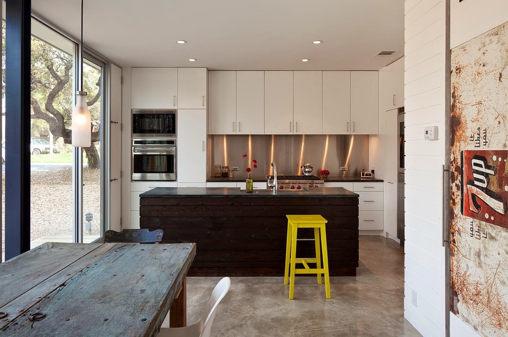 Imagen de cocina contemporánea con armarios con paneles lisos, puertas de armario blancas, salpicadero metalizado, electrodomésticos de acero inoxidable, suelo de cemento y una isla