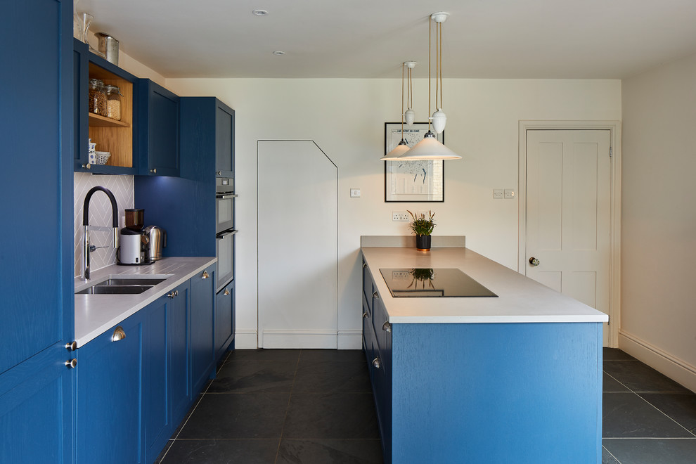Zweizeilige Klassische Küche mit Doppelwaschbecken, Schrankfronten im Shaker-Stil, blauen Schränken, Küchenrückwand in Grau, Halbinsel, grauem Boden, Schieferboden und weißer Arbeitsplatte in London