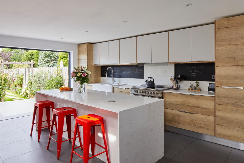 This is an example of a medium sized contemporary galley enclosed kitchen in London with a belfast sink, flat-panel cabinets, light wood cabinets, quartz worktops, white splashback, ceramic flooring, an island, grey floors and white worktops.