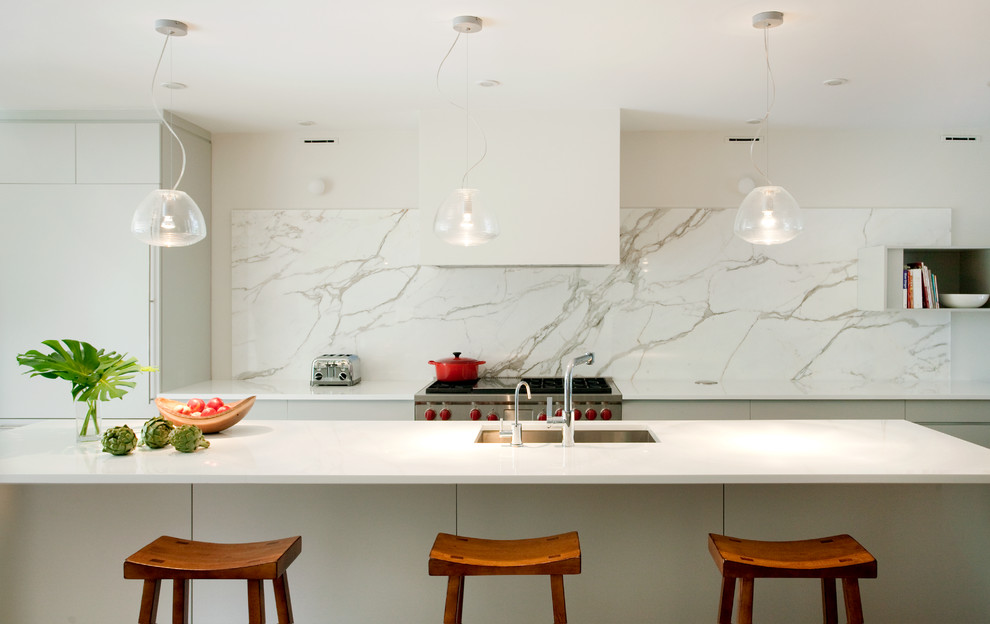 Moderne Wohnküche mit Unterbauwaschbecken, flächenbündigen Schrankfronten, weißen Schränken, Marmor-Arbeitsplatte, Küchenrückwand in Weiß, Rückwand aus Stein, Küchengeräten aus Edelstahl, hellem Holzboden und Kücheninsel in Boston