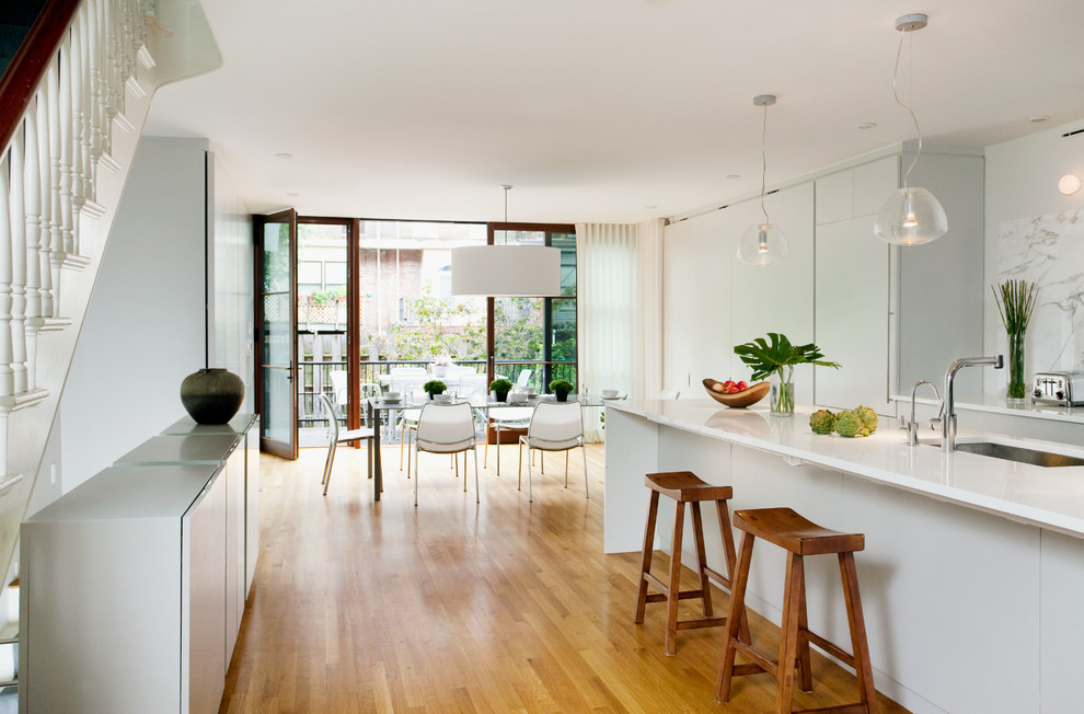 Moderne Wohnküche mit Unterbauwaschbecken, weißen Schränken, Küchenrückwand in Weiß, Rückwand aus Stein, braunem Holzboden, Kücheninsel und Marmor-Arbeitsplatte in Boston