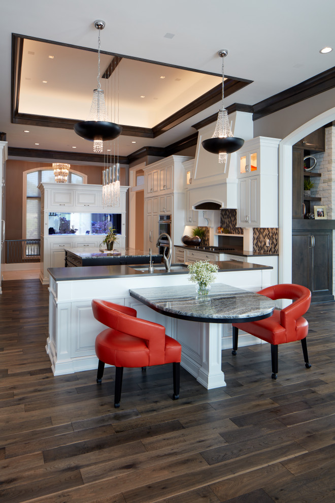 Large transitional u-shaped medium tone wood floor and brown floor kitchen photo in Omaha with an undermount sink, raised-panel cabinets, white cabinets, granite countertops, multicolored backsplash, mosaic tile backsplash, paneled appliances, two islands and gray countertops