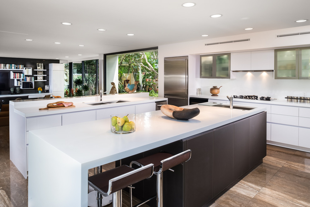 Design ideas for a medium sized contemporary l-shaped kitchen/diner in Miami with a submerged sink, flat-panel cabinets, white cabinets, stainless steel appliances, multiple islands, composite countertops, white splashback, glass sheet splashback and travertine flooring.