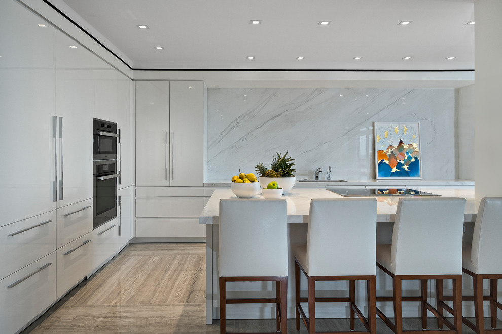 Large contemporary l-shaped open plan kitchen in Miami with a submerged sink, flat-panel cabinets, white cabinets, white splashback, stone slab splashback, integrated appliances, a breakfast bar, brown floors, white worktops and engineered stone countertops.