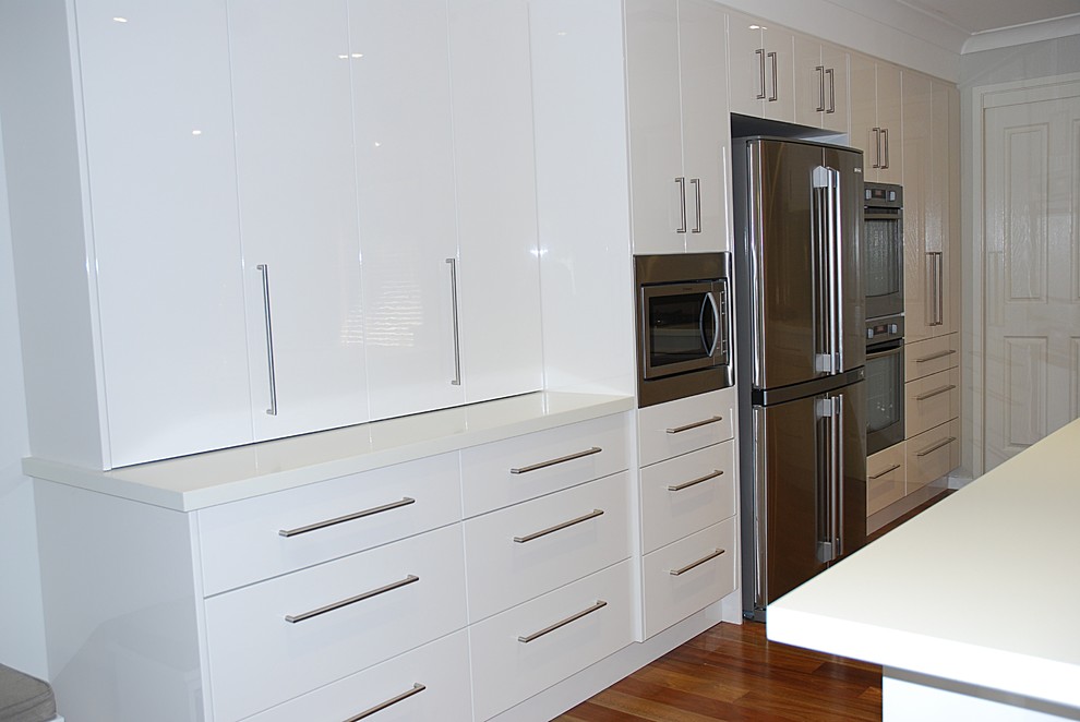 Large minimalist l-shaped medium tone wood floor eat-in kitchen photo in Sydney with an undermount sink, flat-panel cabinets, white cabinets, solid surface countertops, brown backsplash, glass sheet backsplash, stainless steel appliances and an island