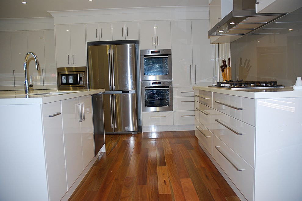 Eat-in kitchen - large modern l-shaped medium tone wood floor eat-in kitchen idea in Sydney with an undermount sink, flat-panel cabinets, white cabinets, solid surface countertops, brown backsplash, glass sheet backsplash, stainless steel appliances and an island