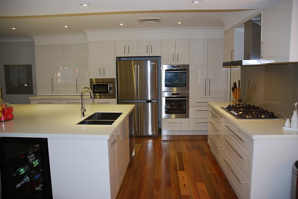 Foto på ett stort funkis kök, med en undermonterad diskho, släta luckor, vita skåp, bänkskiva i koppar, brunt stänkskydd, glaspanel som stänkskydd, rostfria vitvaror, mellanmörkt trägolv och en köksö
