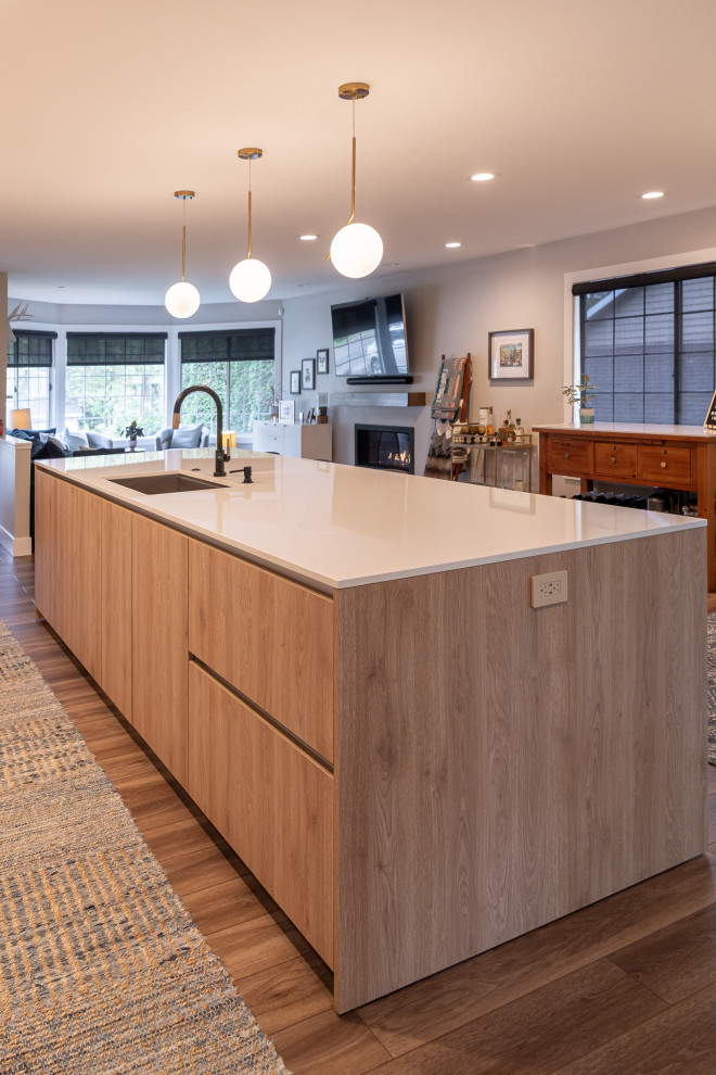 Large contemporary single-wall open plan kitchen in Portland with a submerged sink, flat-panel cabinets, white cabinets, engineered stone countertops, white splashback, engineered quartz splashback, integrated appliances, vinyl flooring, an island, brown floors and white worktops.