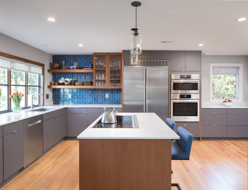 Foto på ett funkis vit kök, med släta luckor, grå skåp, blått stänkskydd, rostfria vitvaror, en köksö och ljust trägolv